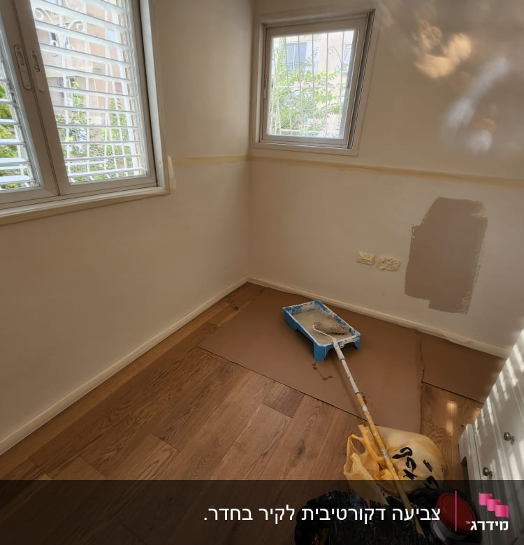 חדר עם קיר צבוע חלקית, מגש צבע ומברשת על הרצפה